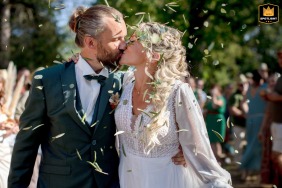 Bride and groom kissing at the end of the ceremony in La Pacaudiere, France, surrounded by sunshine and flying confetti.